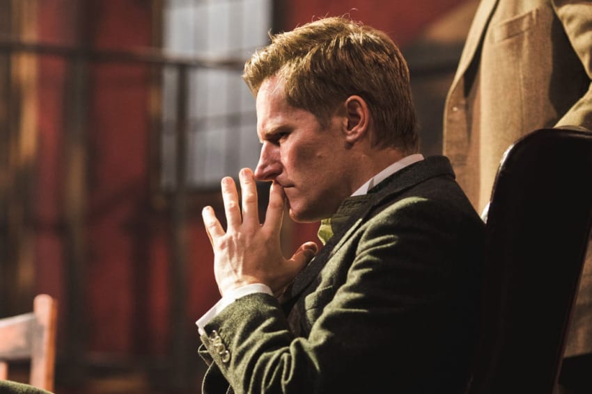 A production image from ‘Sherlock Holmes – The Hunt for Moriarty.’ A man sits in a chair. He is holding both hands close to his face, clearly deep in thought about something.