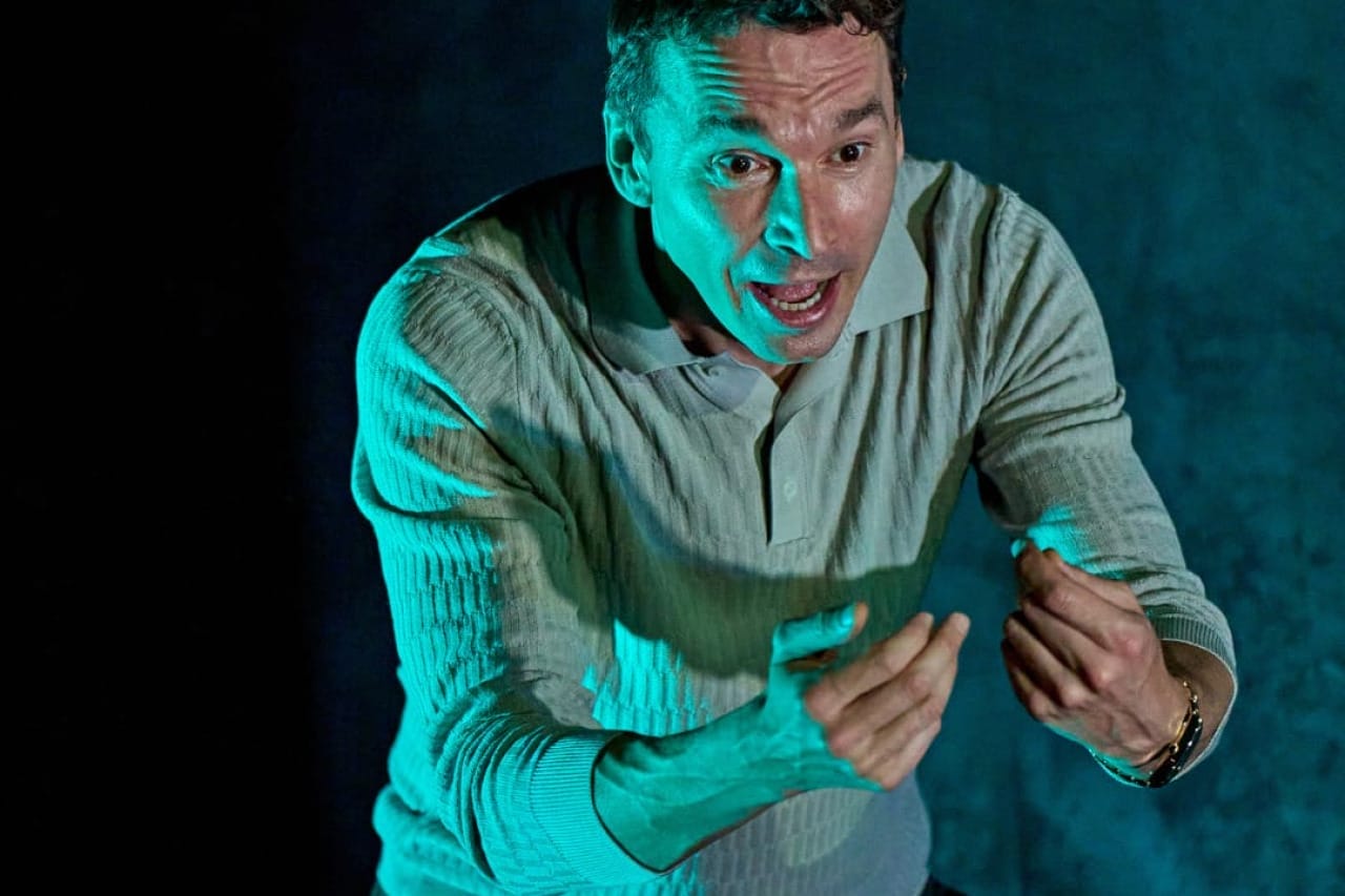 A production image from ‘Don’t Look Now.’ John is shouting, with a terrified look on his face, and is throwing his arms out in front of him. He is lit from the left in blue lighting.