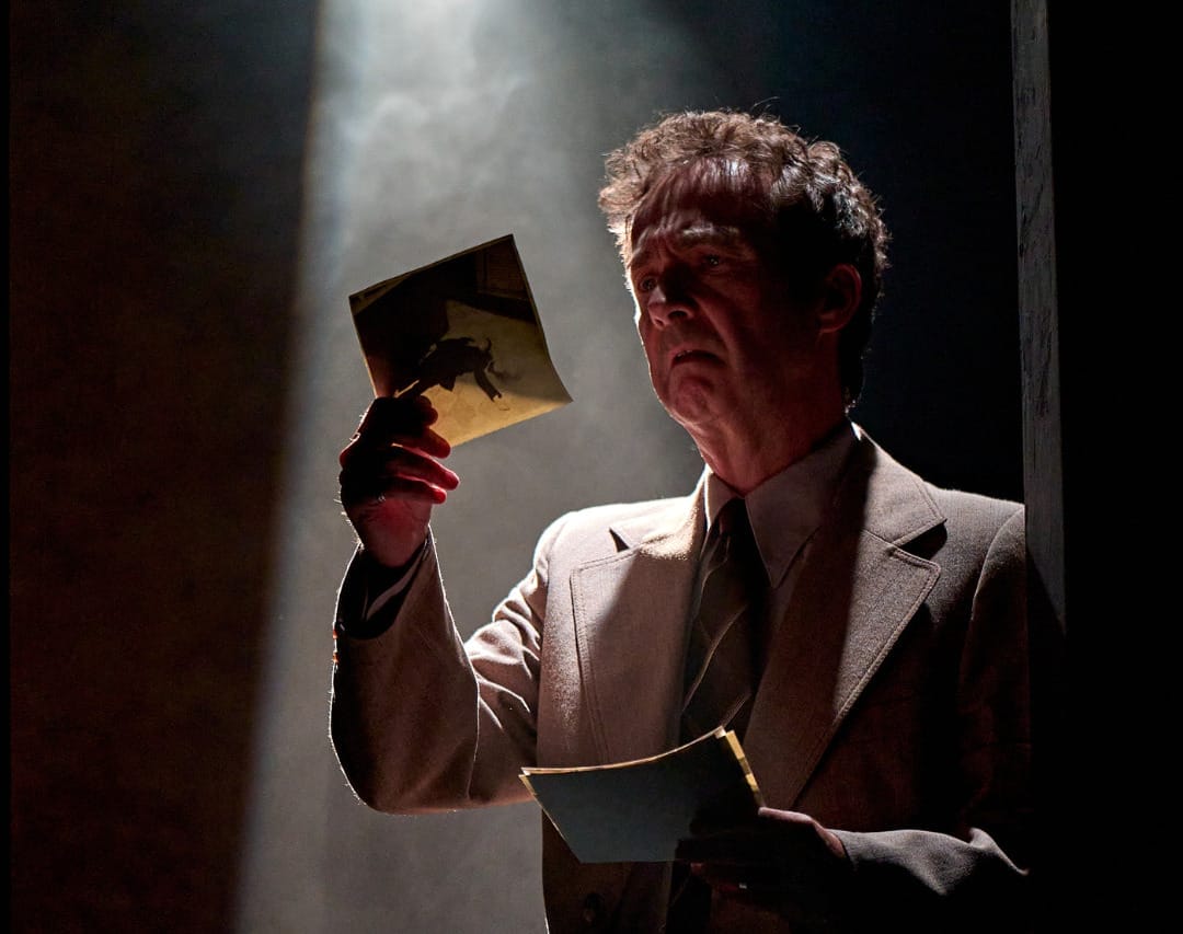 A production image from ‘Don’t Look Now.’ A man stands in a spotlight, looking concerned as he looks at a piece of paper which he holds in his right hand.