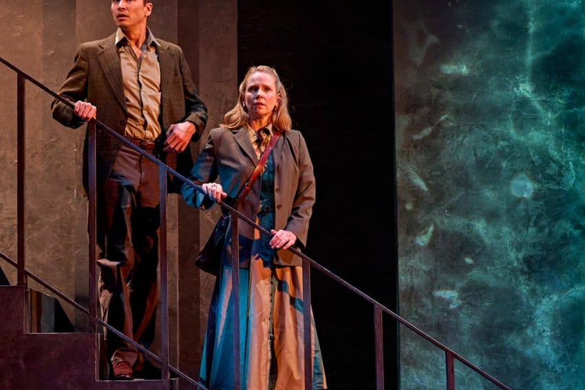 A production image from ‘Don’t Look Now.’ John and Laura stand half-way down some stairs, holding onto the railings. They both have slightly stunned looks on their faces, as if they have been spooked by a sight or a sound.